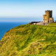 Historic stone tower overlooking the Atlantic Ocean on a green Irish cliff with visitors gathered at the base
